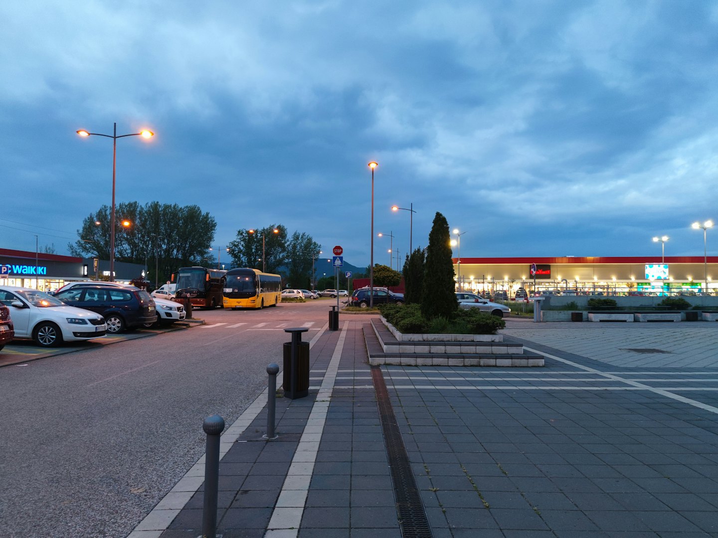 Cars and buses park in a busy shopping center lot.